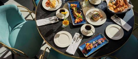 A round table with a variety of dishes, including croissants and fruit, and a small vase with sunflowers.