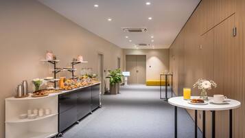 Un corredor moderno de hotel con una barra de desayuno, una zona de estar y una pequeña mesa con bebidas y pasteles.