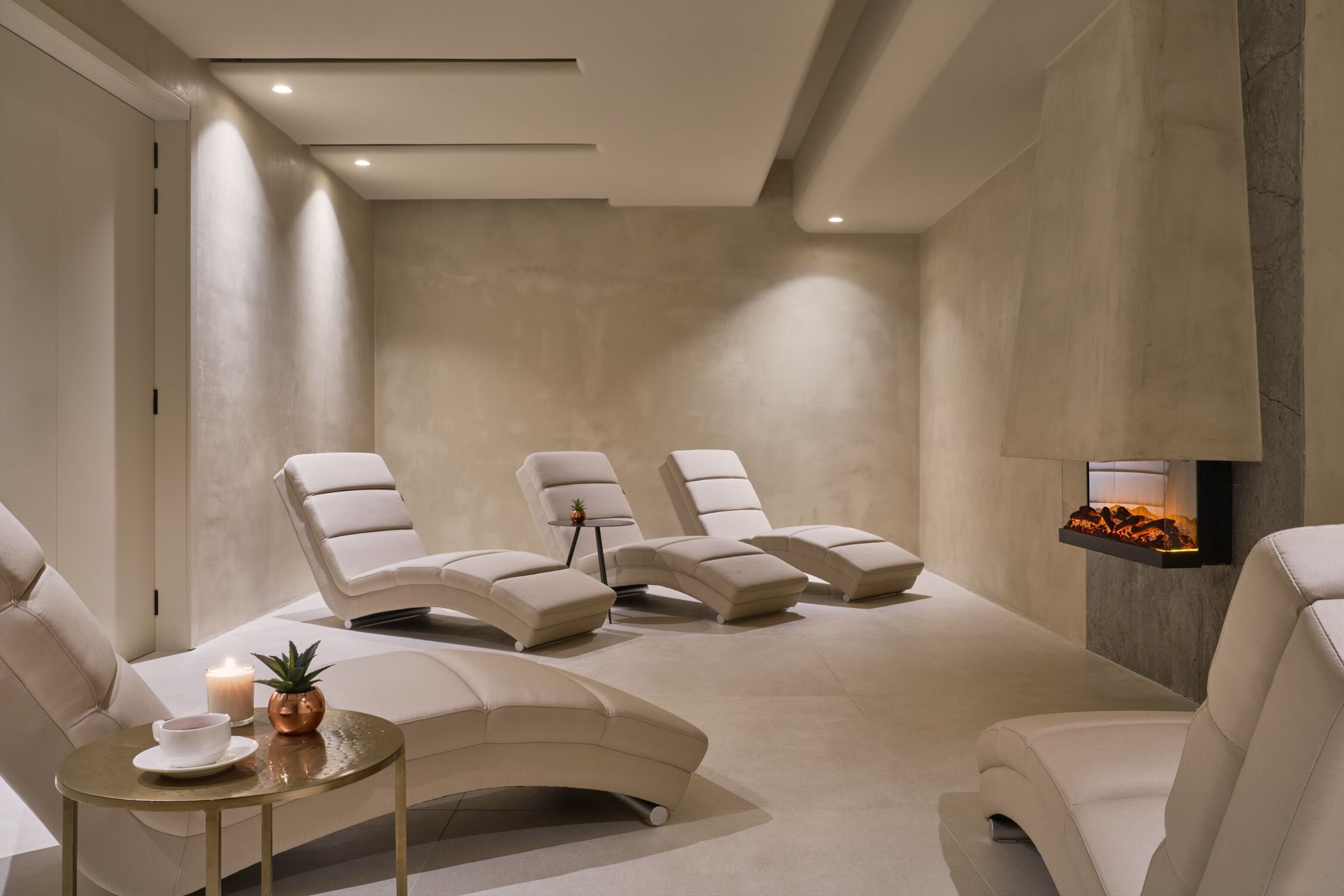 Un cuarto de spa con sillones reclinables, una mesita con una vela y una planta, y una chimenea empotrada en la pared.