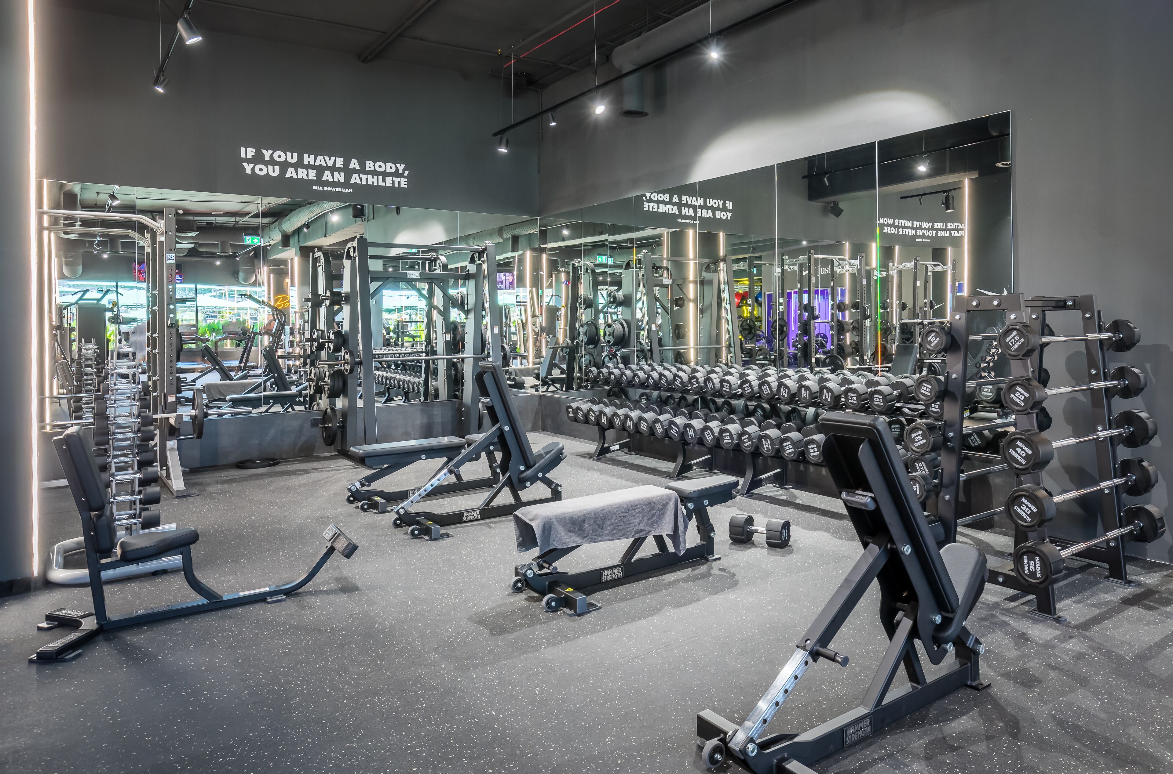 A modern gym with various weightlifting equipment, mirrors, and motivational quotes on the walls.