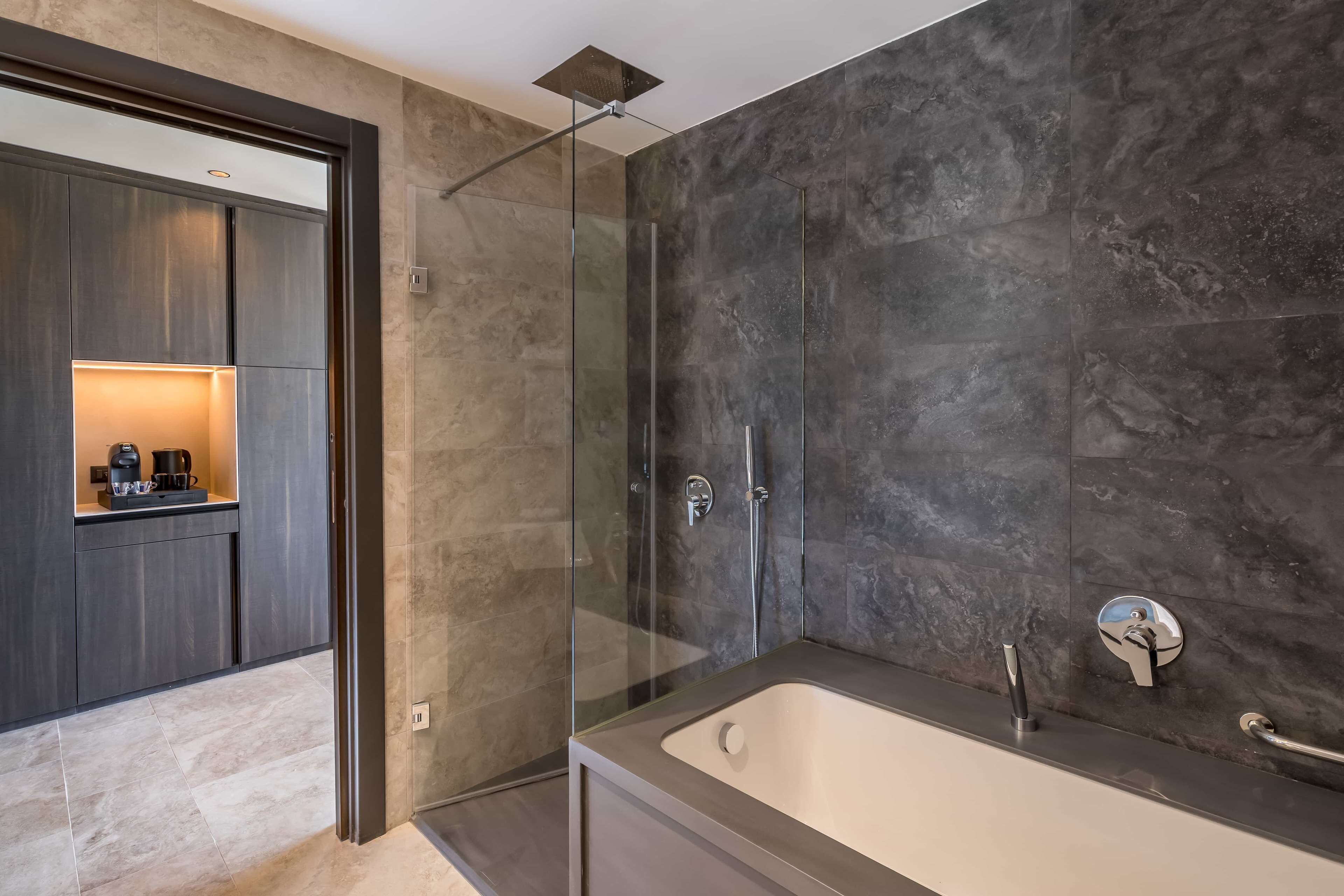 A modern bathroom with a glass-enclosed shower, a freestanding bathtub, and a dark wood vanity with a built-in coffee maker.