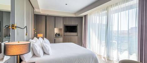 Een moderne hotelkamer met een groot bed, een bureau met lamp, een televisie en een balkon met gordijnen.