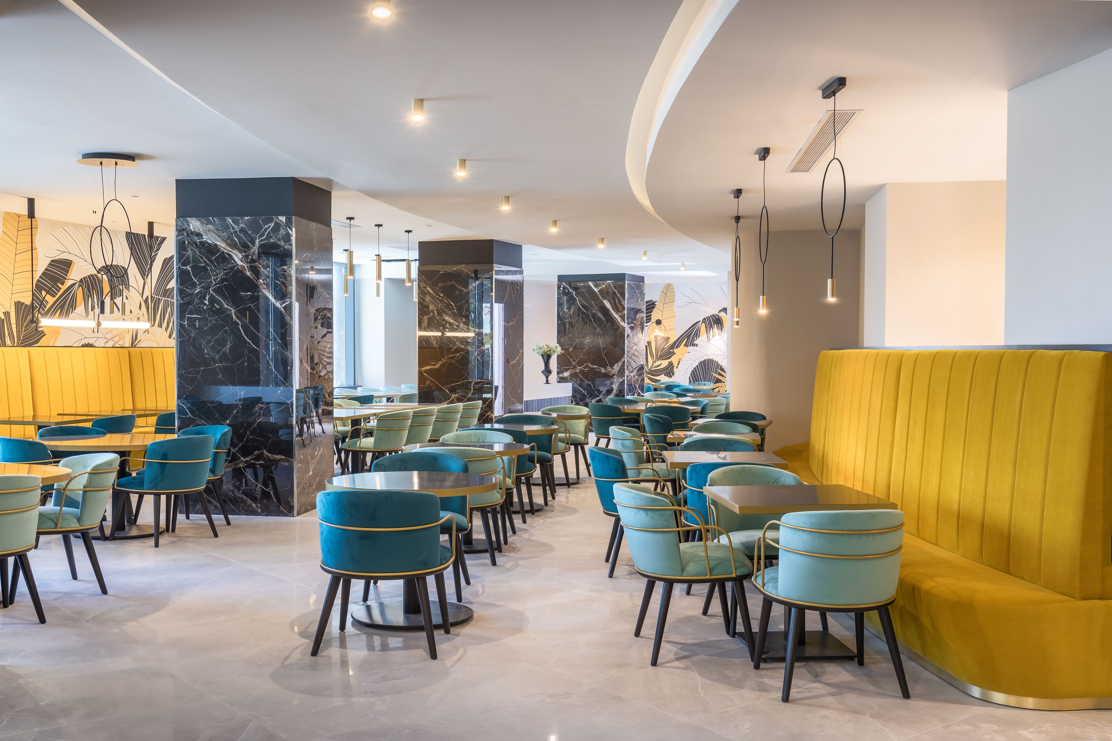 Un comedor moderno con paredes de mármol, asientos amarillos y azules, e iluminación colgante.