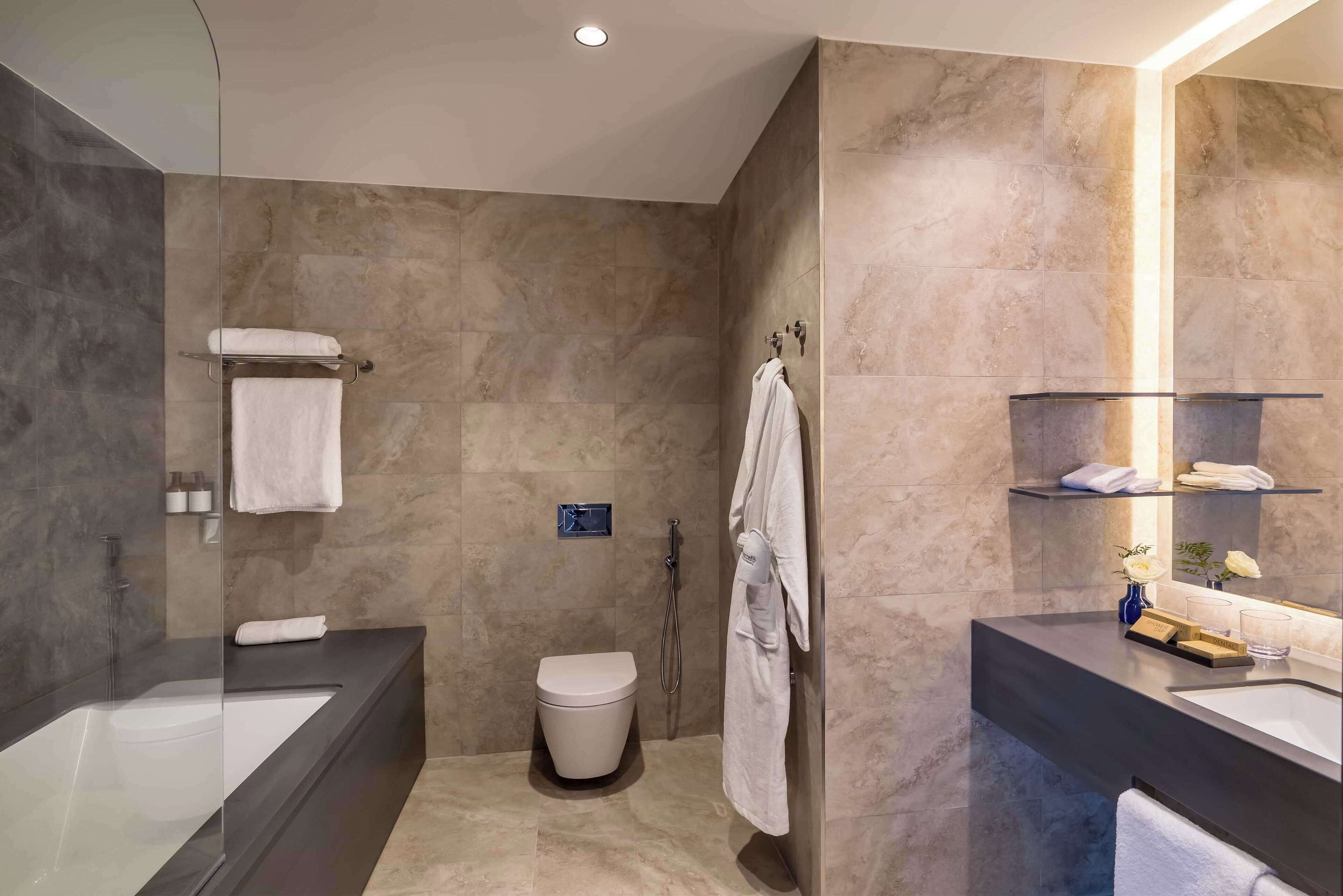 Un baño moderno con bañera de hidromasaje con mampara de vidrio, inodoro separado y zona de ducha.