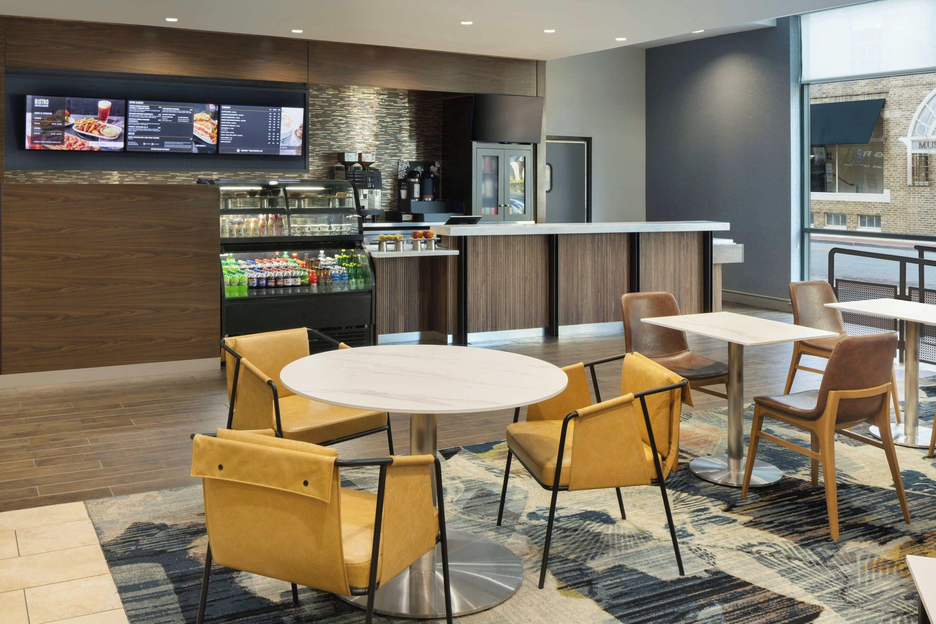 Un moderno hall de hotel con zona de bar, arreglos de asientos y una pantalla digital con el menú.