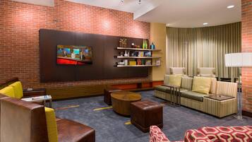 A modern hotel lobby with a brick wall, a flat-screen TV, seating areas, and a bookshelf.