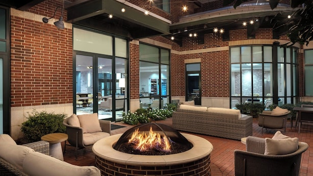 A patio area with a fire pit, wicker furniture, and a brick wall. - Courtyard by Marriott Little Rock Downtown (Little Rock)