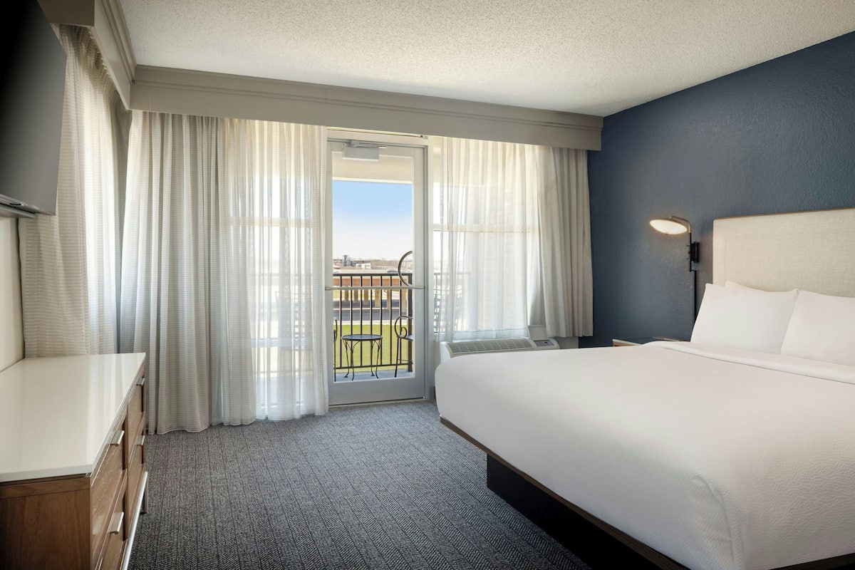 Ein Hotelzimmer mit einem großen Bett, einem Schreibtisch und Blick ins Freie durch eine Schiebetür.