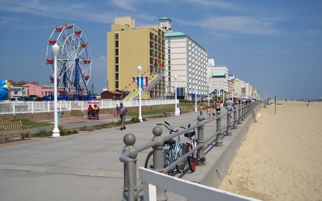 A boardwalk with a Ferris wheel, a building with a green roof, and a beach in the background.
