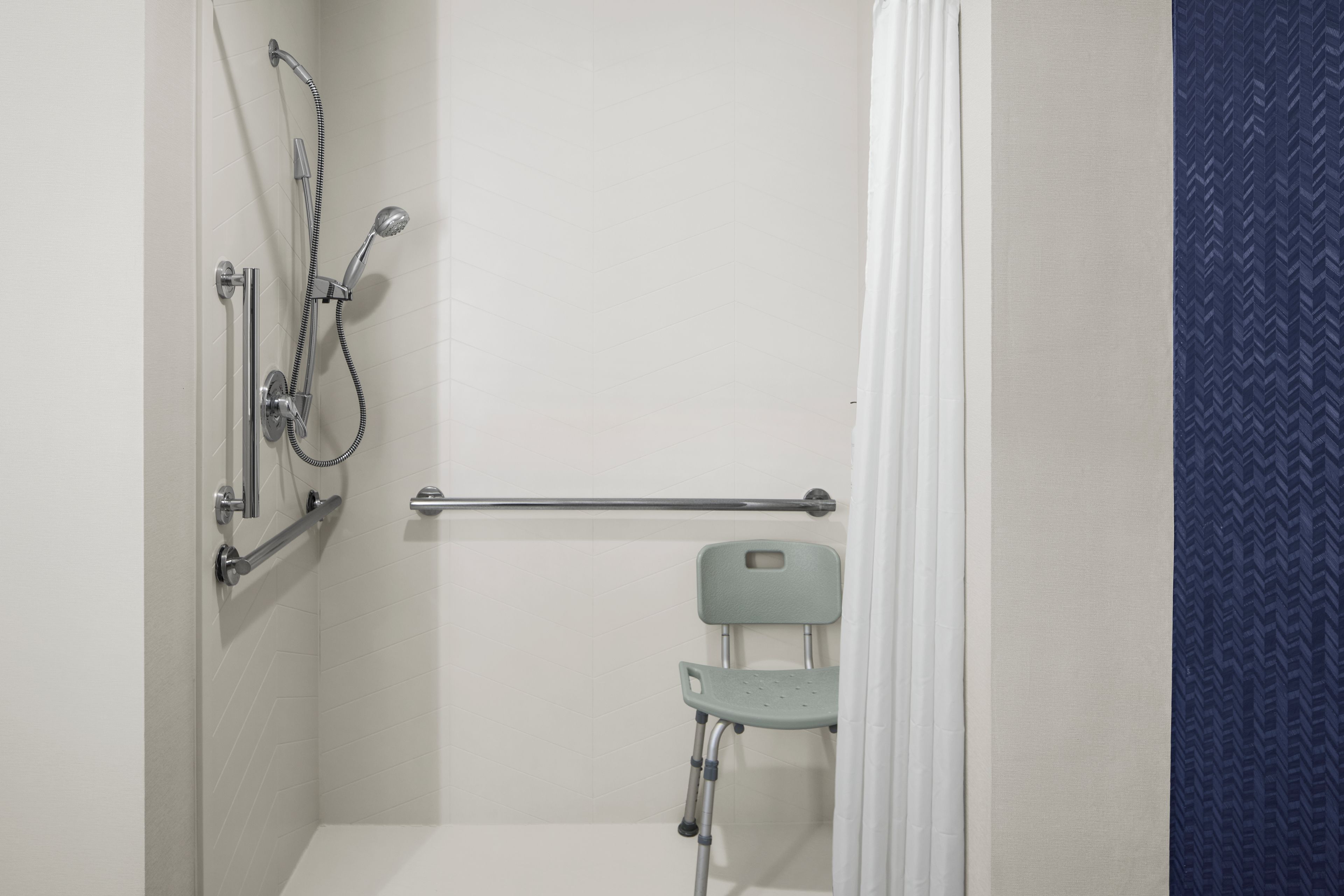 A bathroom with a shower, grab bar, and a wheelchair-accessible chair.
