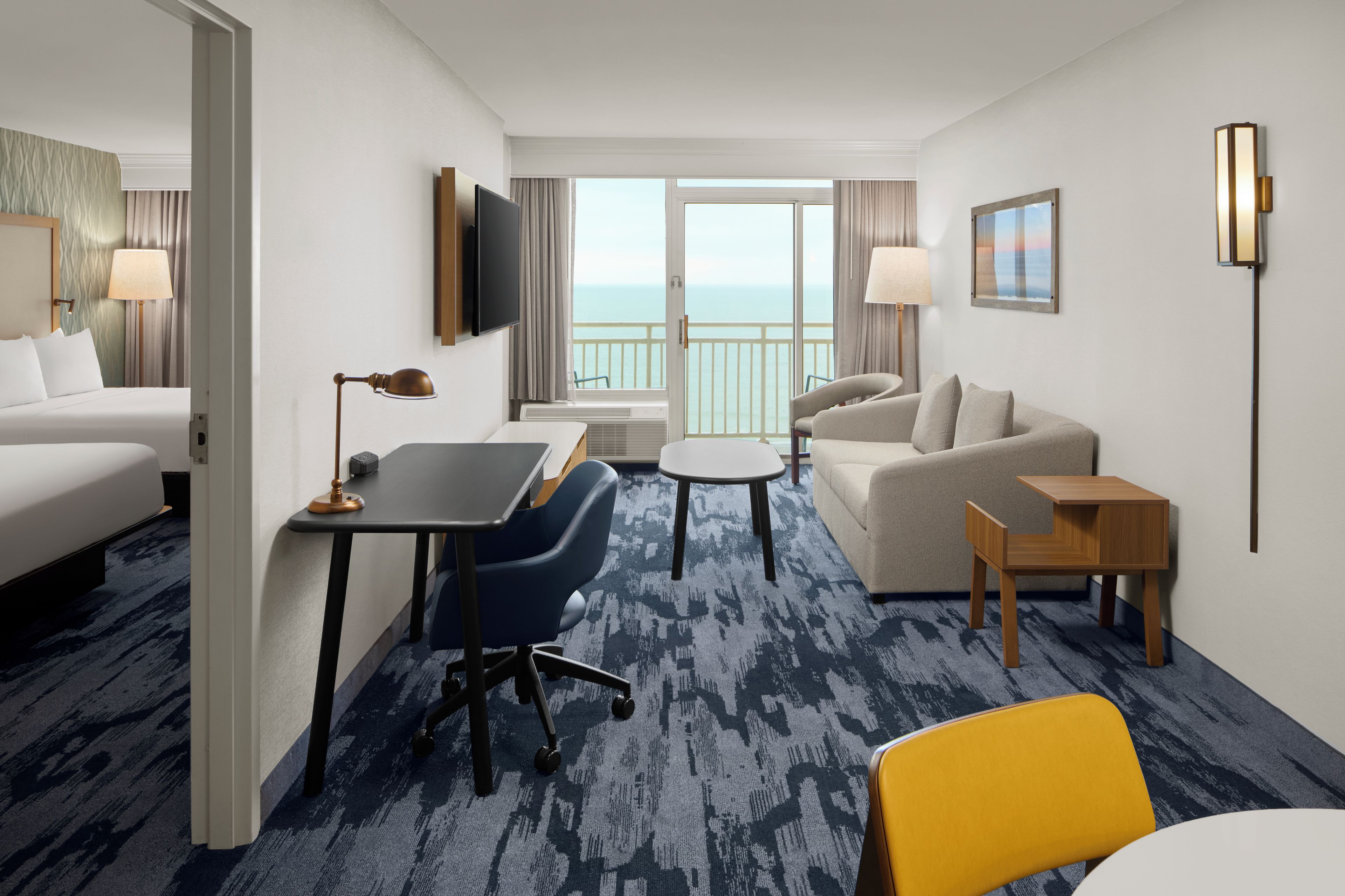 Habitación de hotel con cama, escritorio, sofá, silla y balcón con vista al mar.