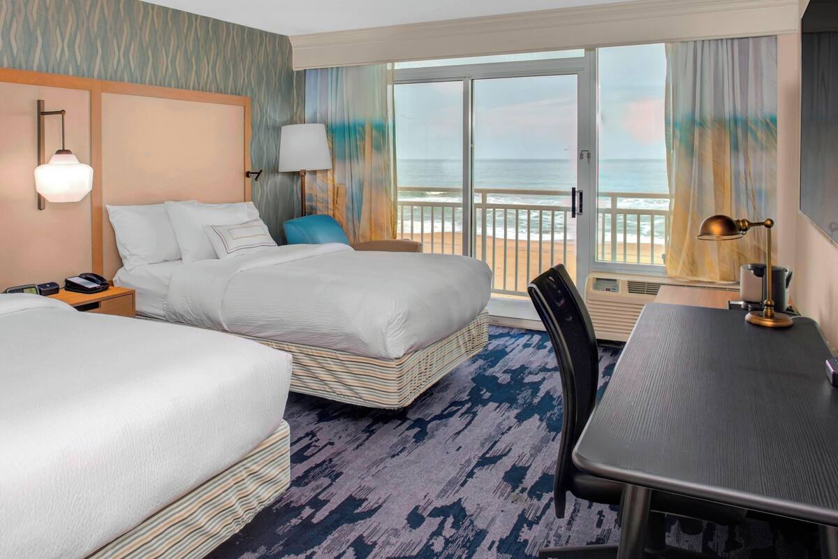 A hotel room with two beds, a desk, and a view of the ocean.