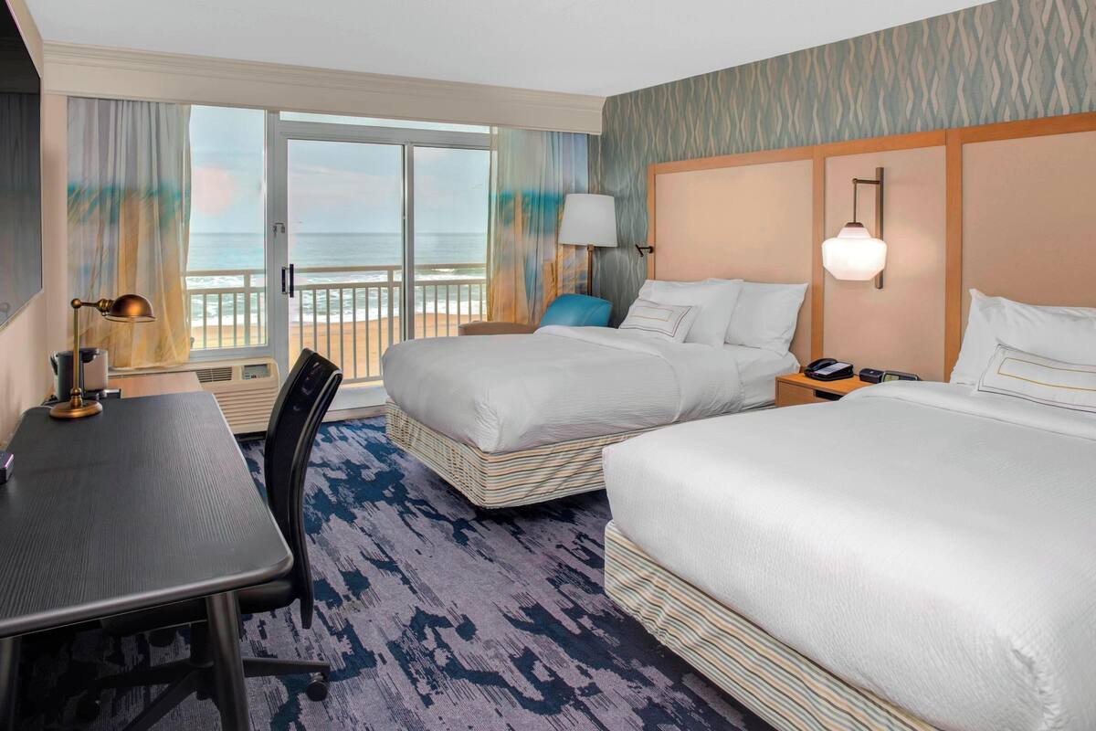 A hotel room with two beds, a desk, and a view of the ocean.