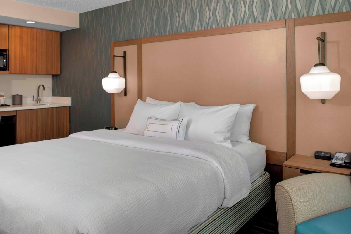 A hotel room with a bed, bedside tables, a desk with a microwave, and a chair.