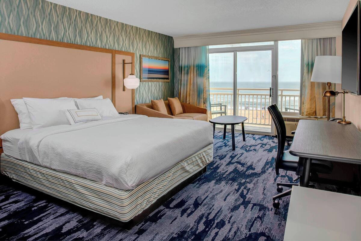 A hotel room with a large bed, a sofa, a small table, and a view of the beach.