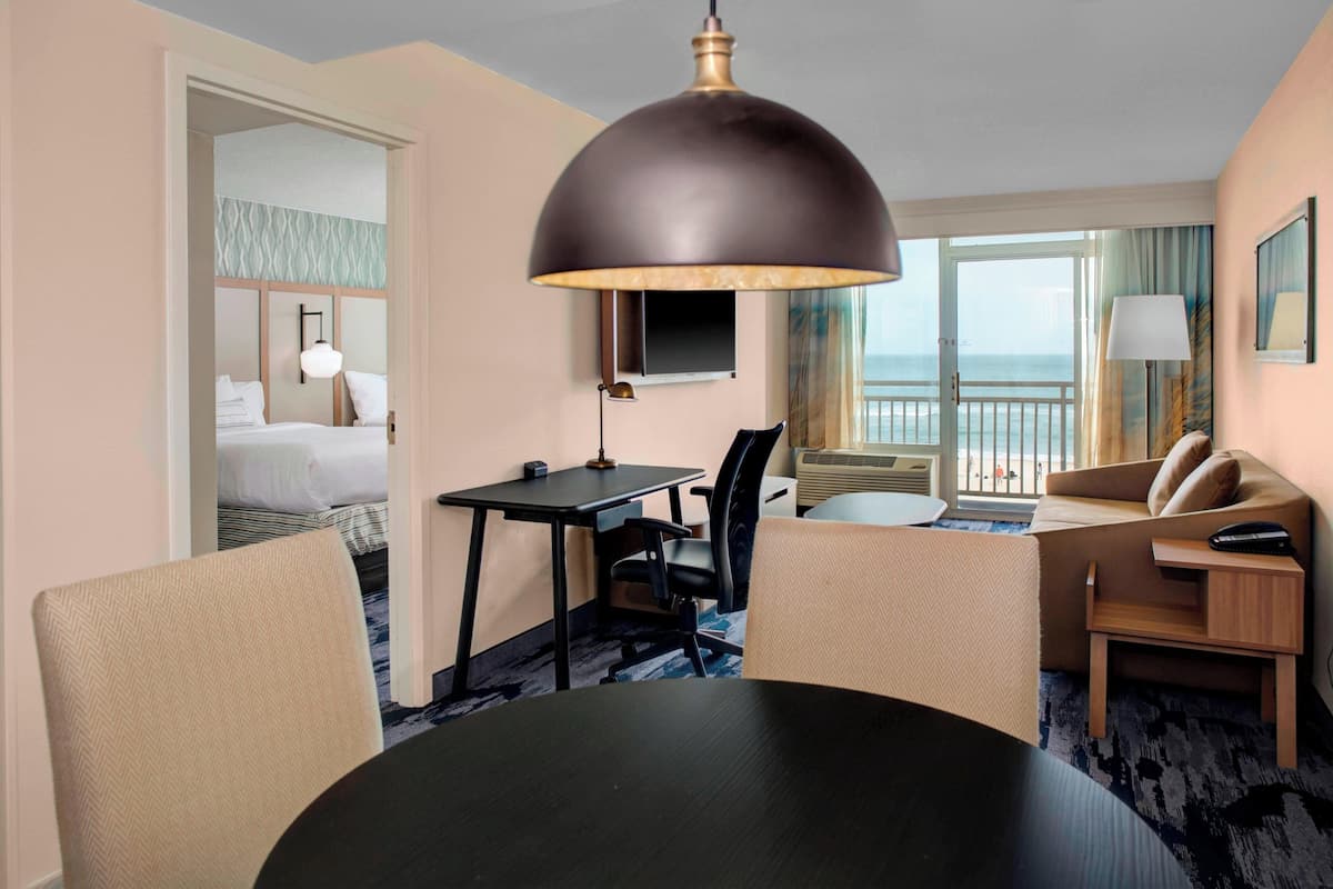 A hotel room with a bed, a desk, a chair, a sofa, a TV, and a balcony with a view.