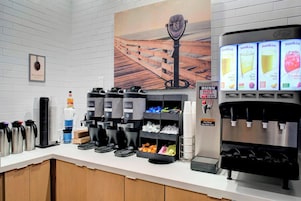 Um espaço com estação de café, vários dispensadores de café, um refrigerador de água e um dispensador de suco.