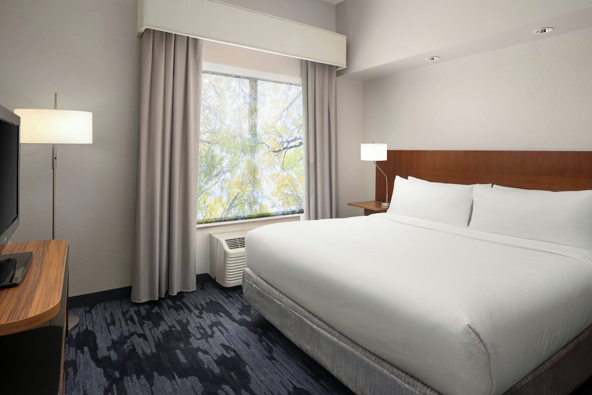 A hotel room with a large bed, a desk with a lamp, a TV, and a window with curtains.