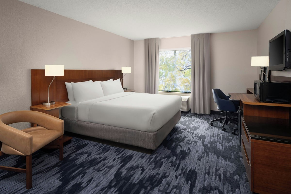 A hotel room with a large bed, a desk with a television, a chair, and a window with curtains.