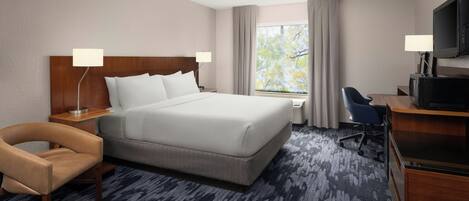 A hotel room with a large bed, a desk with a television, a chair, and a window with curtains.
