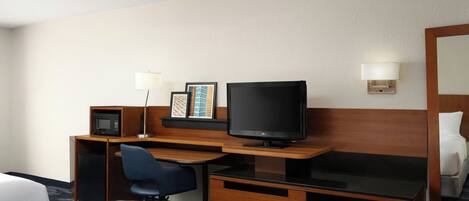 A hotel room with a bed, a desk with a computer, a television, and a microwave.