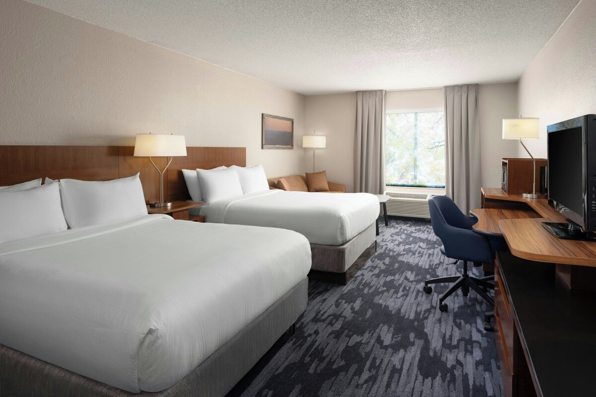A hotel room with two beds, a desk, a television, and a window with curtains.