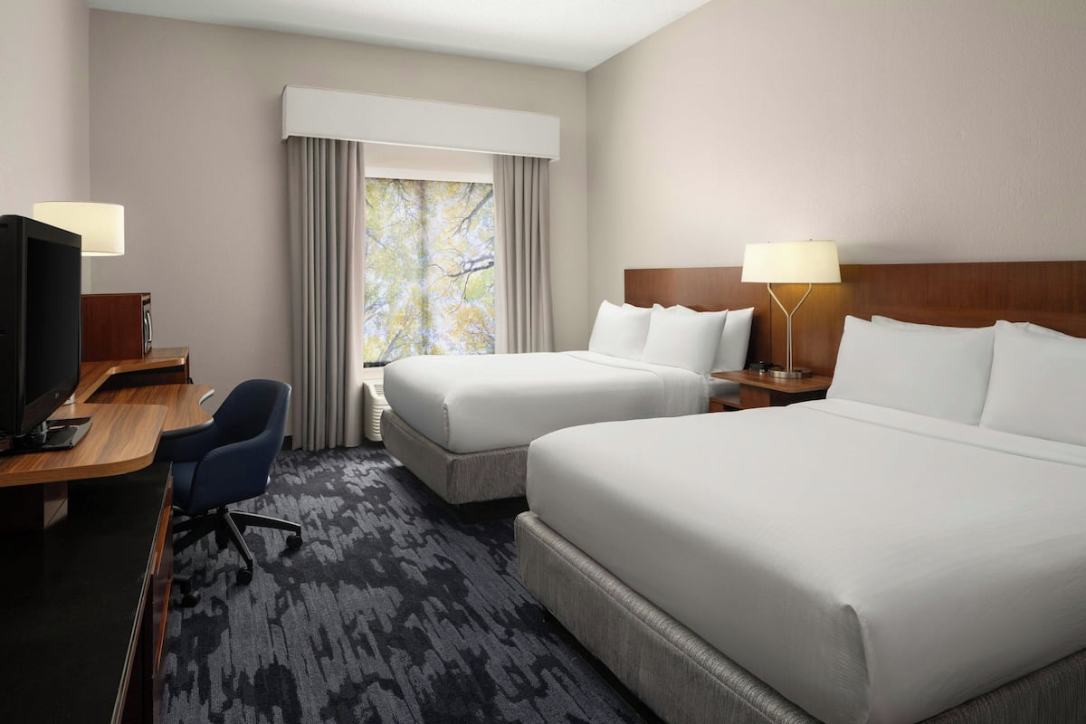 A hotel room with two beds, a desk with a computer, a chair, and a window with curtains.