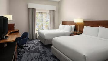 A hotel room with two beds, a desk with a computer, a chair, and a window with curtains.