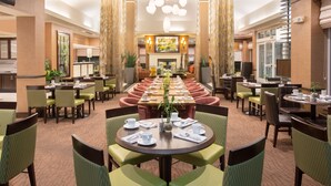 A spacious hotel lobby with a long dining table, multiple seating areas, and a central fireplace. - Hilton Garden Inn Salt Lake City/Layton (Layton)