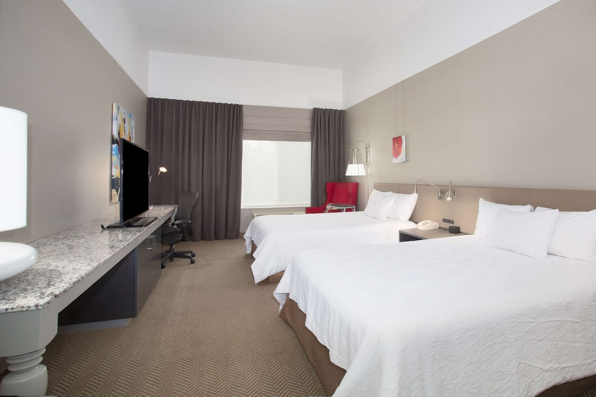 A hotel room with two beds, a desk with a computer, a chair, a TV, and a window with curtains.