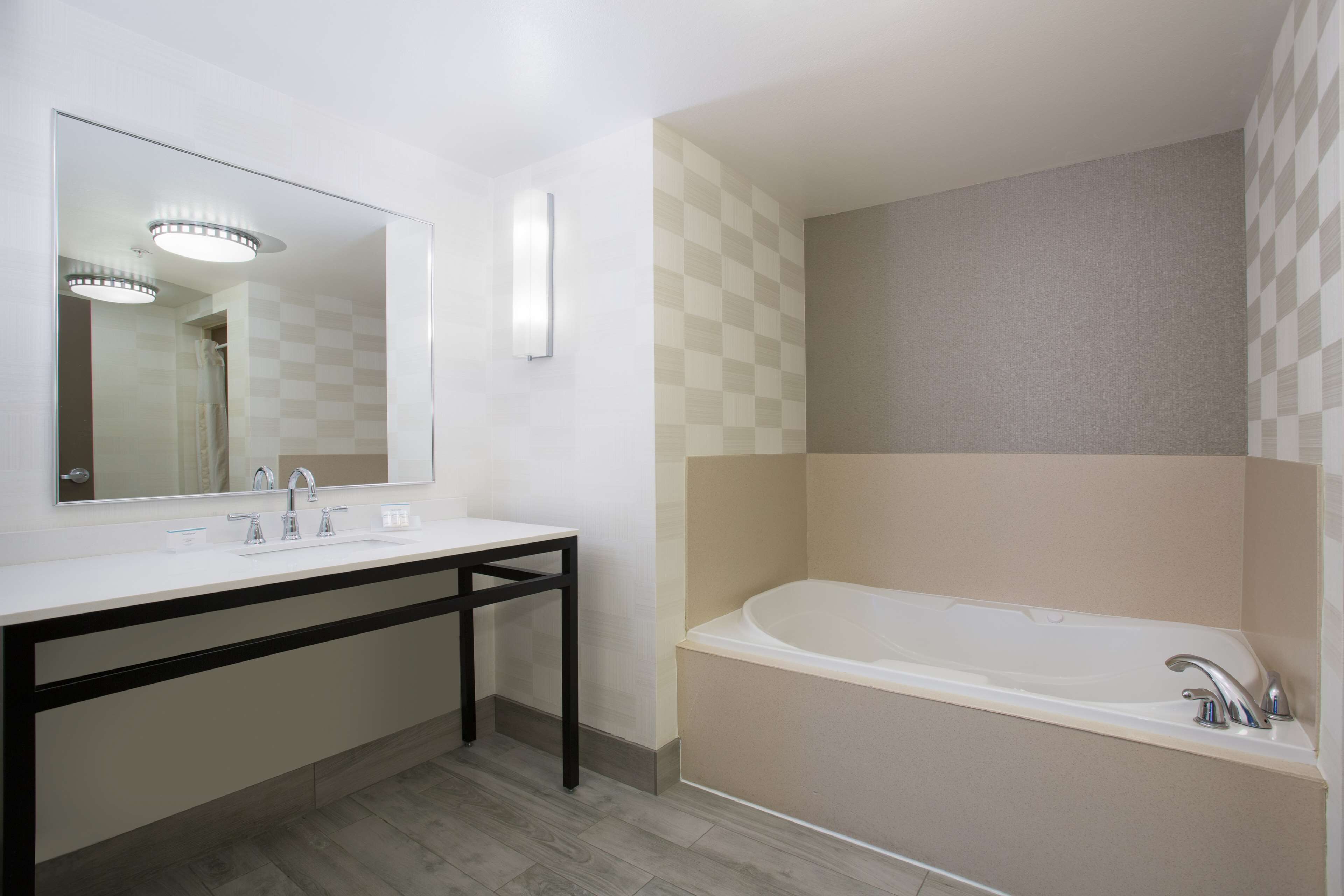Un baño moderno con un espejo grande, un lavamanos blanco, un mueble de tocador negro y una bañera independiente.