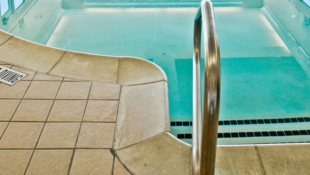 An indoor swimming pool with clear blue water, surrounded by white chairs and potted plants. - Hilton Garden Inn Salt Lake City/Layton (Layton)