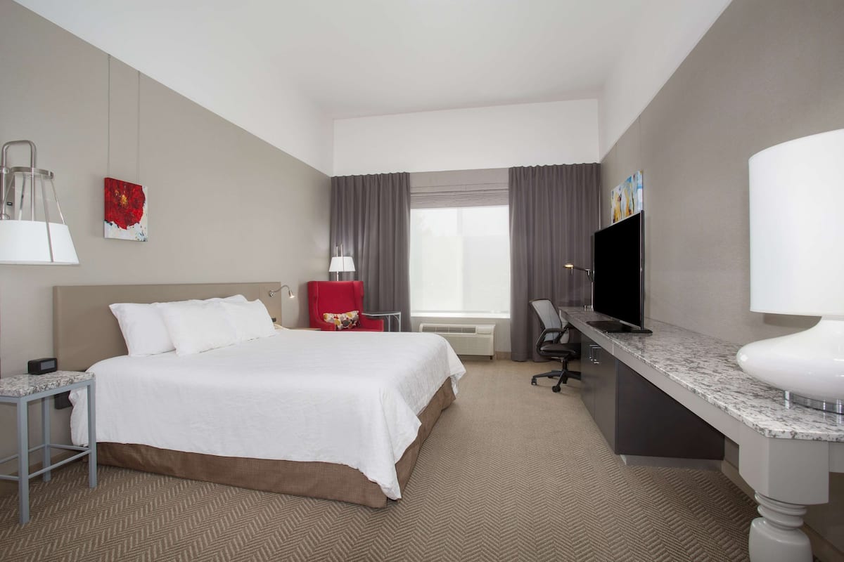 A hotel room with a bed, desk, chair, TV, and a window with curtains.