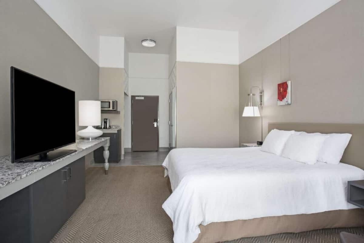 A hotel room with a bed, a TV, a desk with a lamp, a microwave, and a door.