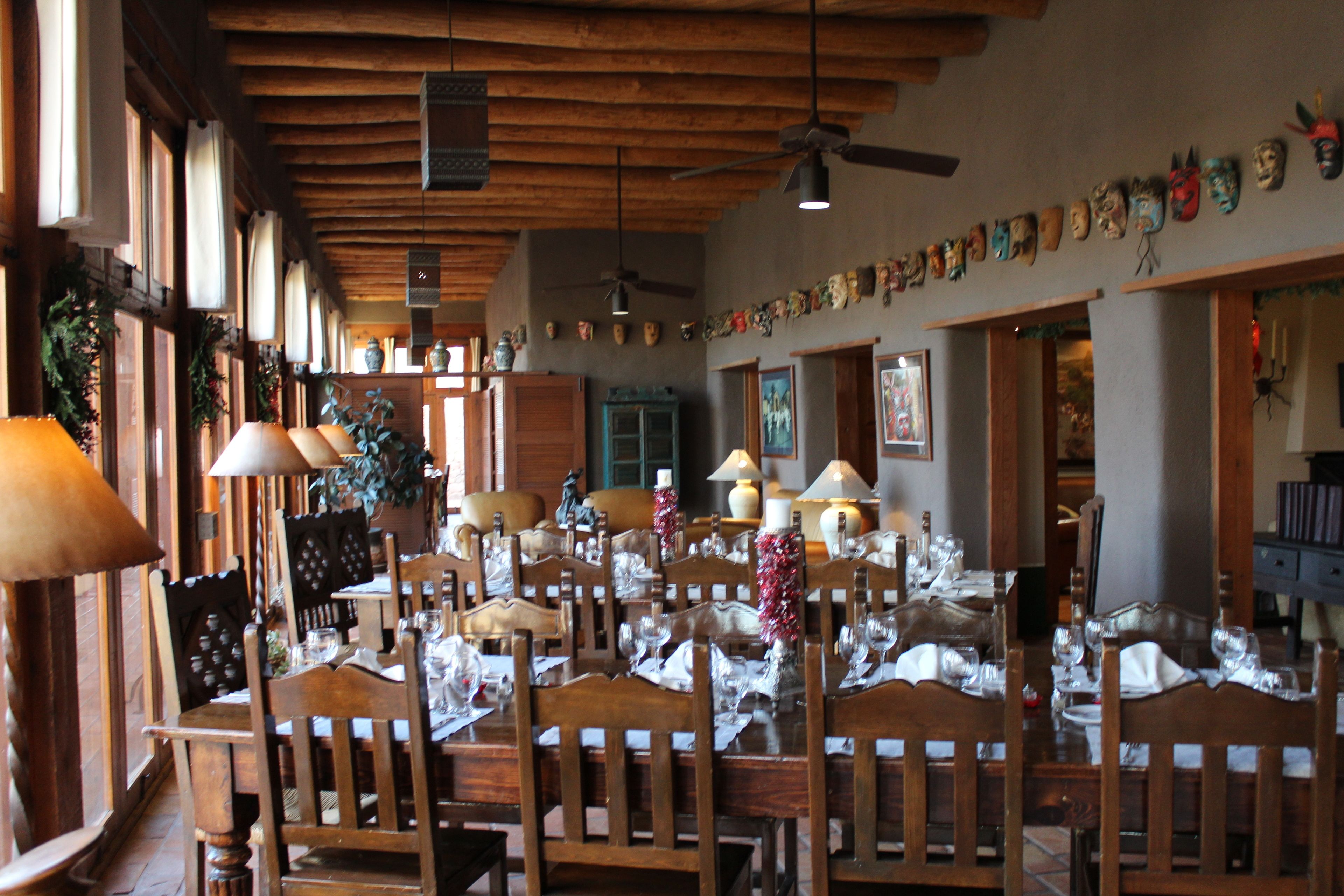 A dining area with wooden tables and chairs, ceiling fans, and a wall decorated with masks.