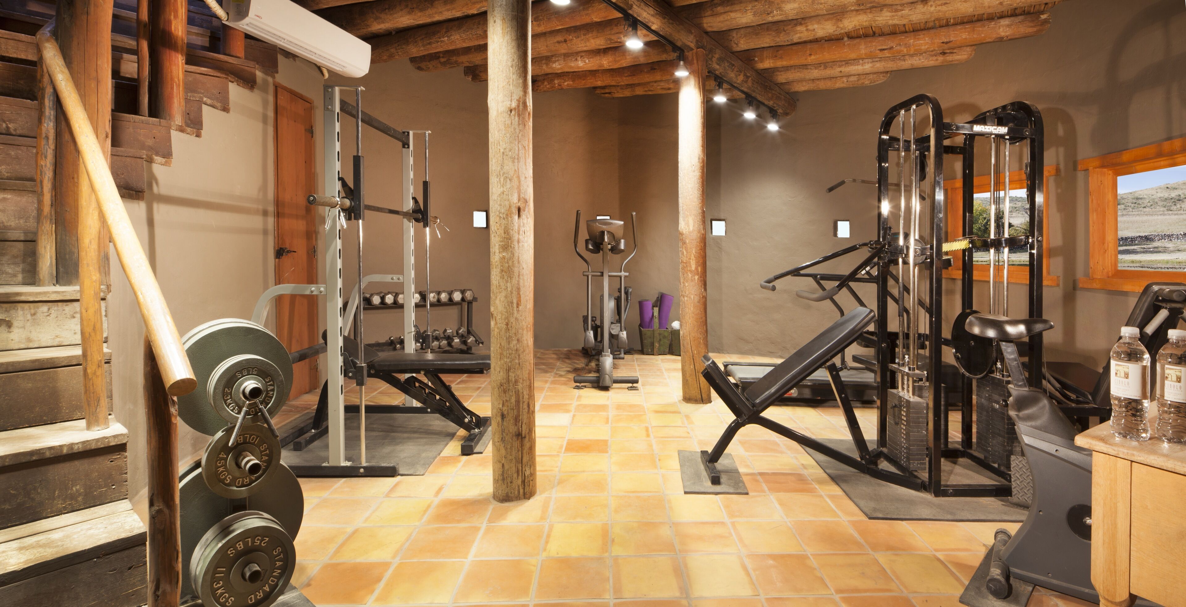 A gym with various exercise equipment, wooden beams on the ceiling, and a tiled floor.