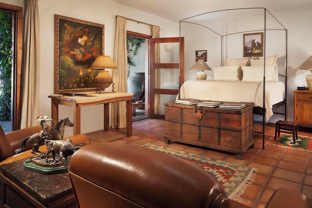 Una habitación con una cama, un aparador, un escritorio con una lámpara y un cuadro en la pared.