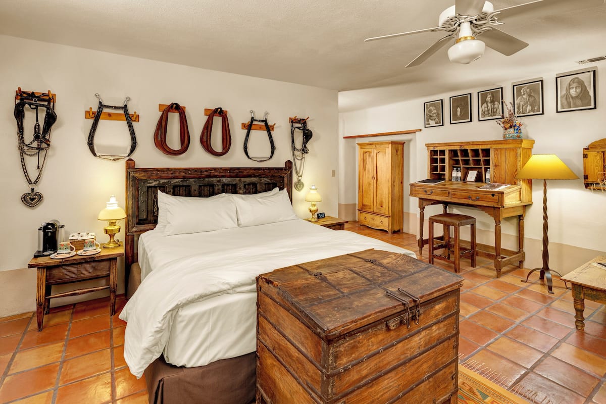 Un dormitorio con una cama de madera, un escritorio, una silla, una lámpara y un aparador.