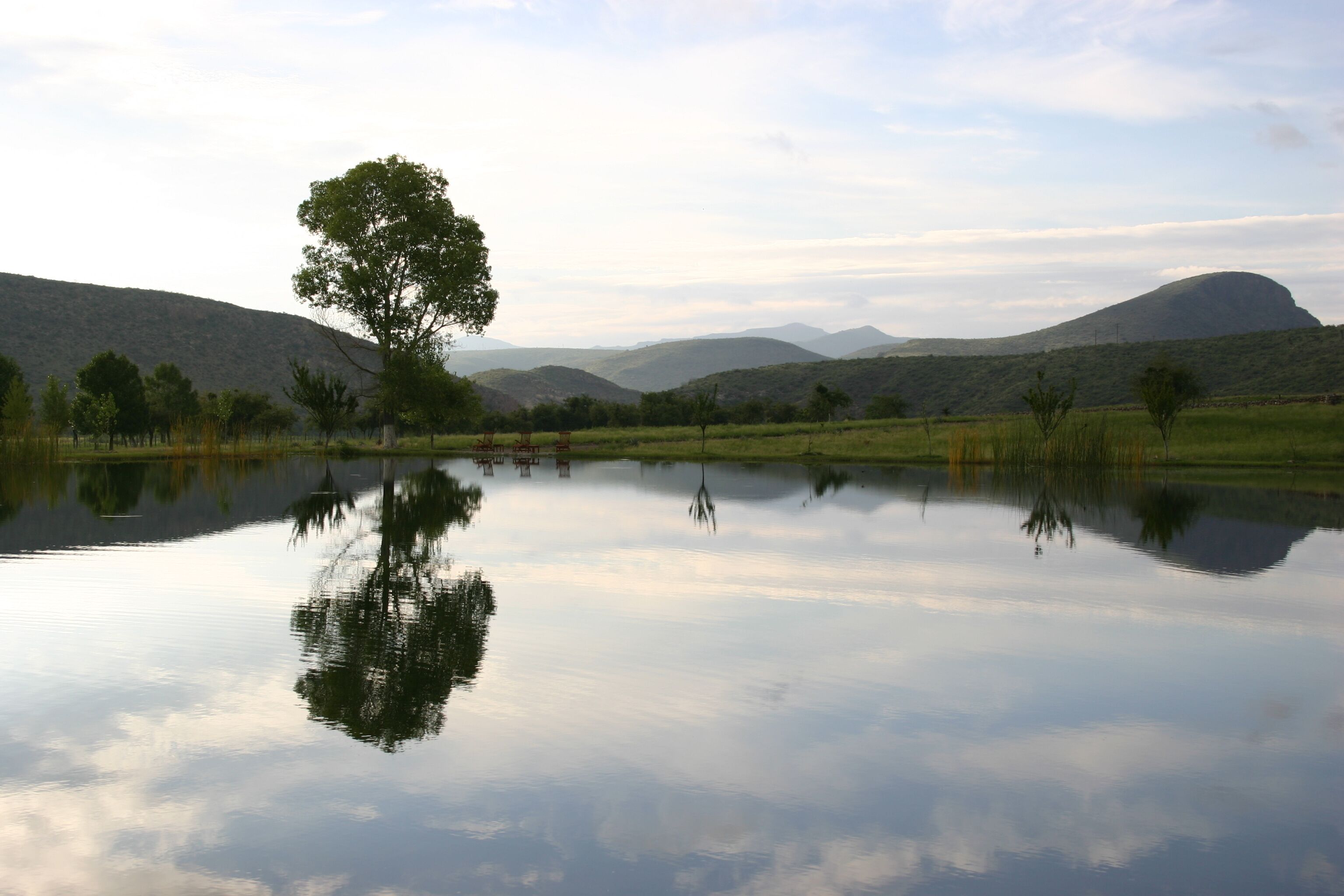 Un lago tranquilo con reflejos de árboles y colinas al fondo.