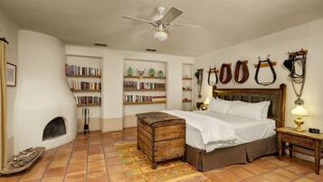 A bedroom with a bed, a wooden chest, a fireplace, bookshelves, and horse tack on the wall.