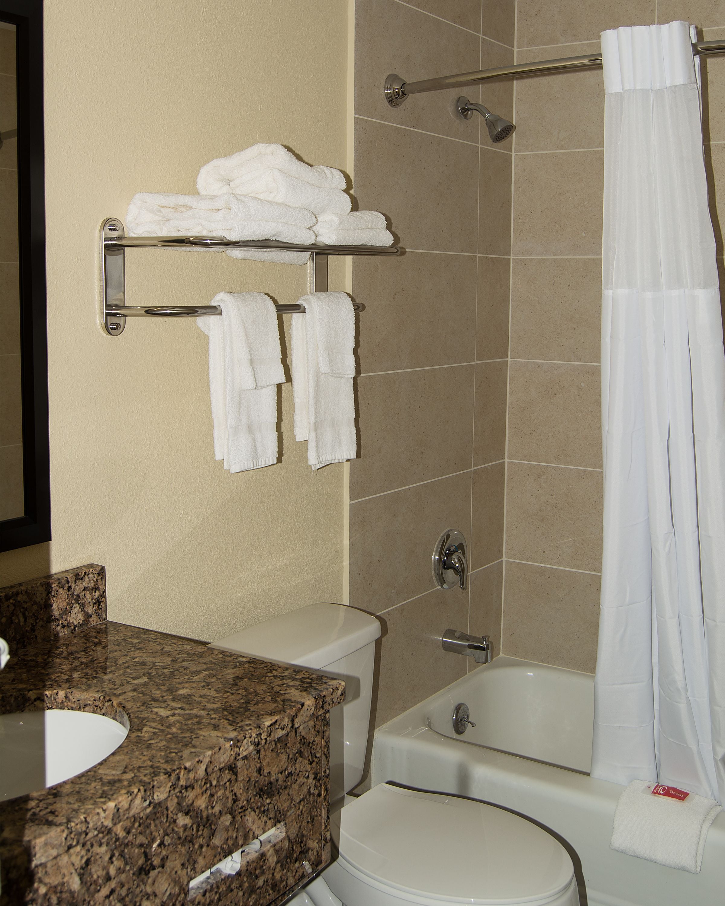 A bathroom with a granite countertop sink, a toilet, a bathtub, and a shower curtain.