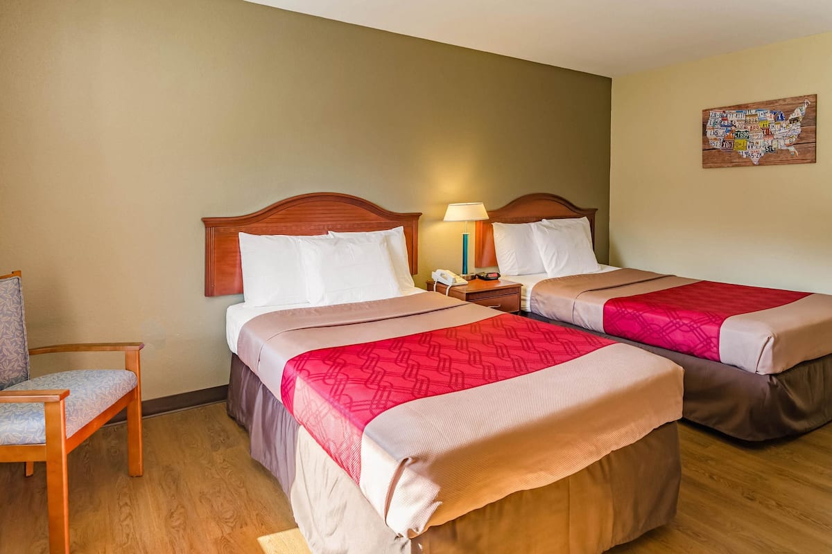 Une chambre d’hôtel avec deux lits, une table de chevet, une lampe et une chaise.