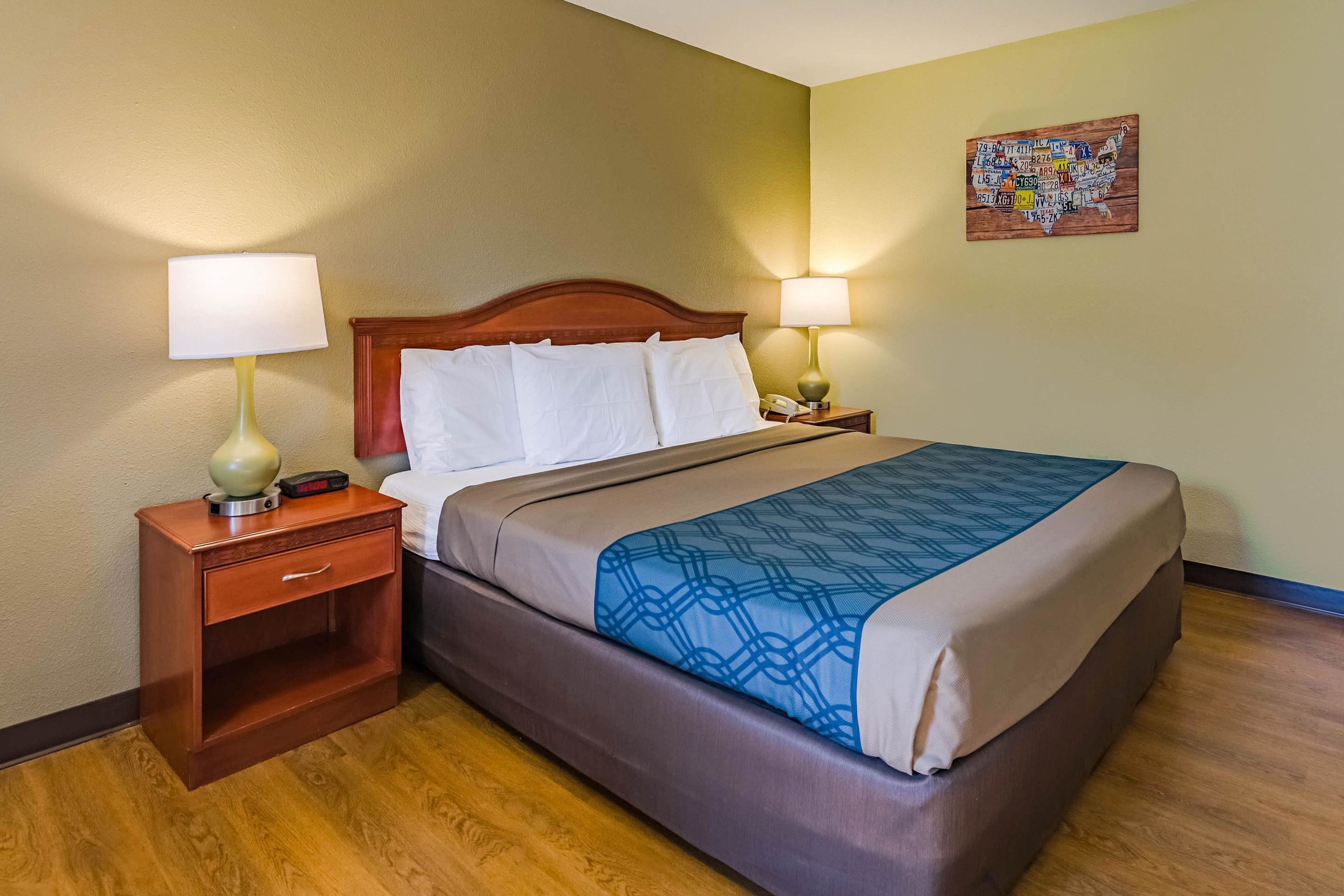 A hotel room with a bed, two bedside tables, a nightstand, and a wall art piece.