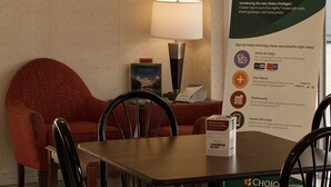 Un espace repas d’hôtel avec une table et des chaises, un tableau encadré au mur et une affiche faisant la promotion du programme de fidélité Choice Privileges.