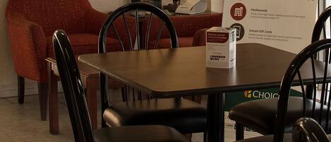 A hotel dining area with a table and chairs, a framed picture on the wall, and a poster advertising Choice Privileges.