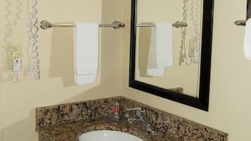 Un baño con encimera de granito, un lavamanos blanco, un espejo y un secador de pelo fijado a la pared.