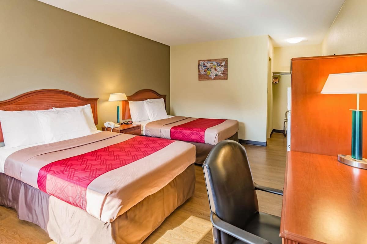 Une chambre d’hôtel avec deux lits, un bureau, une chaise et une table de chevet avec une lampe.