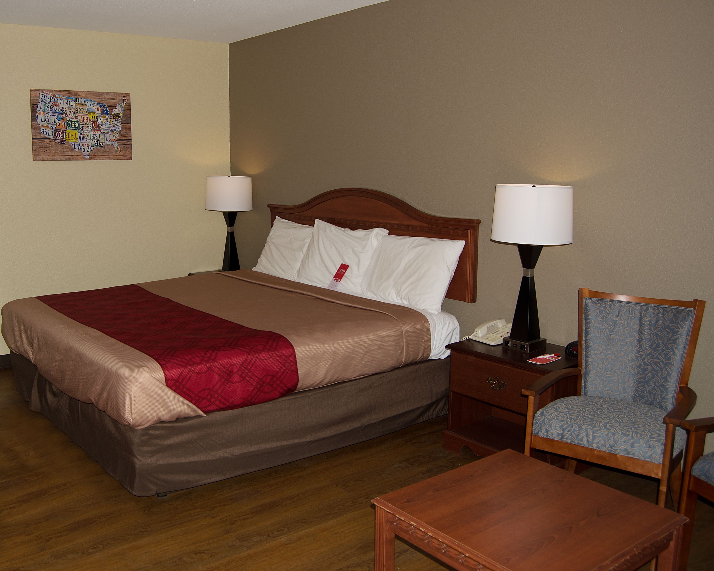 A hotel room with a large bed, two bedside lamps, a wooden nightstand, a chair, and a wooden table.