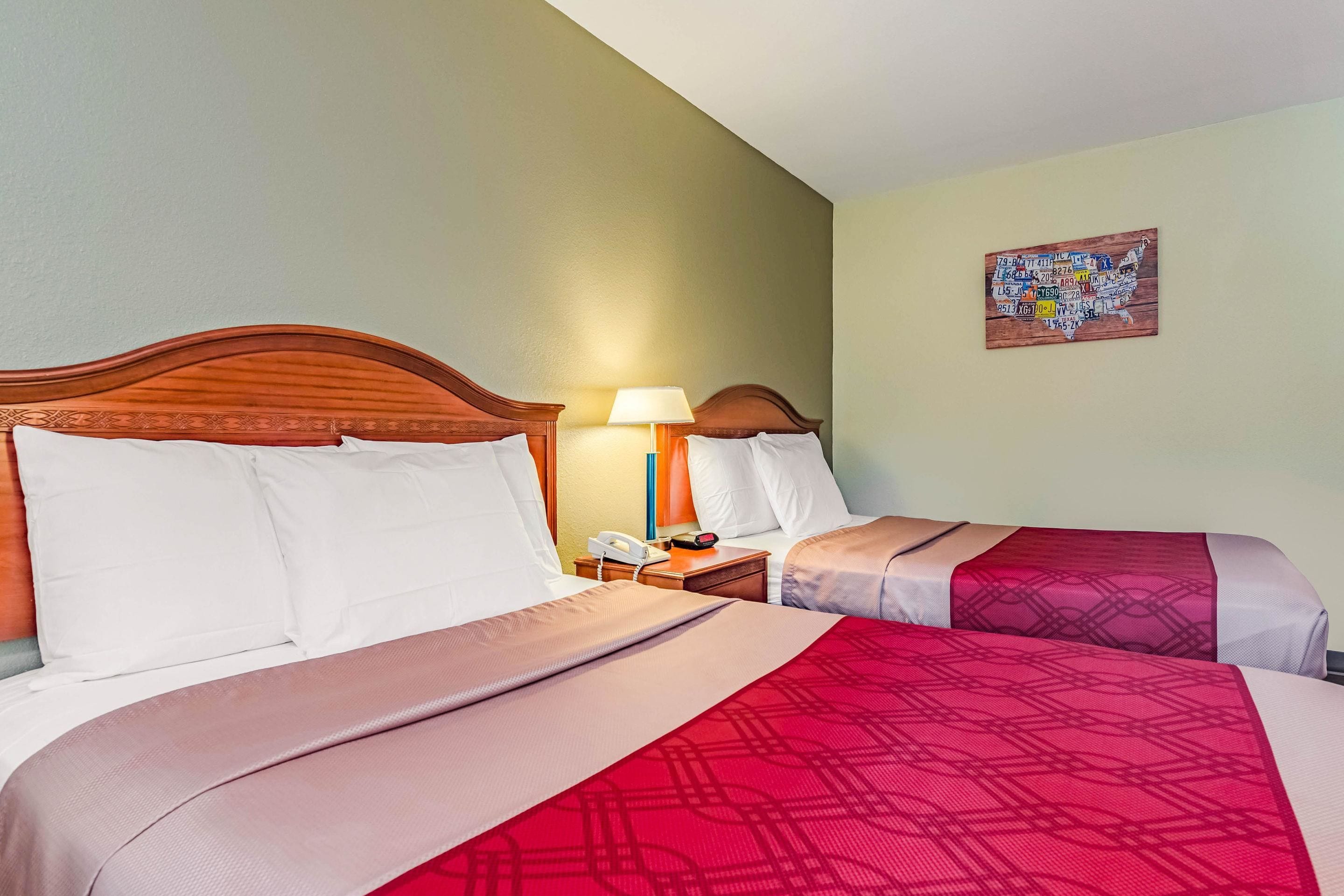 Hotelkamer met twee bedden, een houten hoofdbord, wit beddengoed, een nachtkastje met een lamp en een wereldkaart aan de muur.