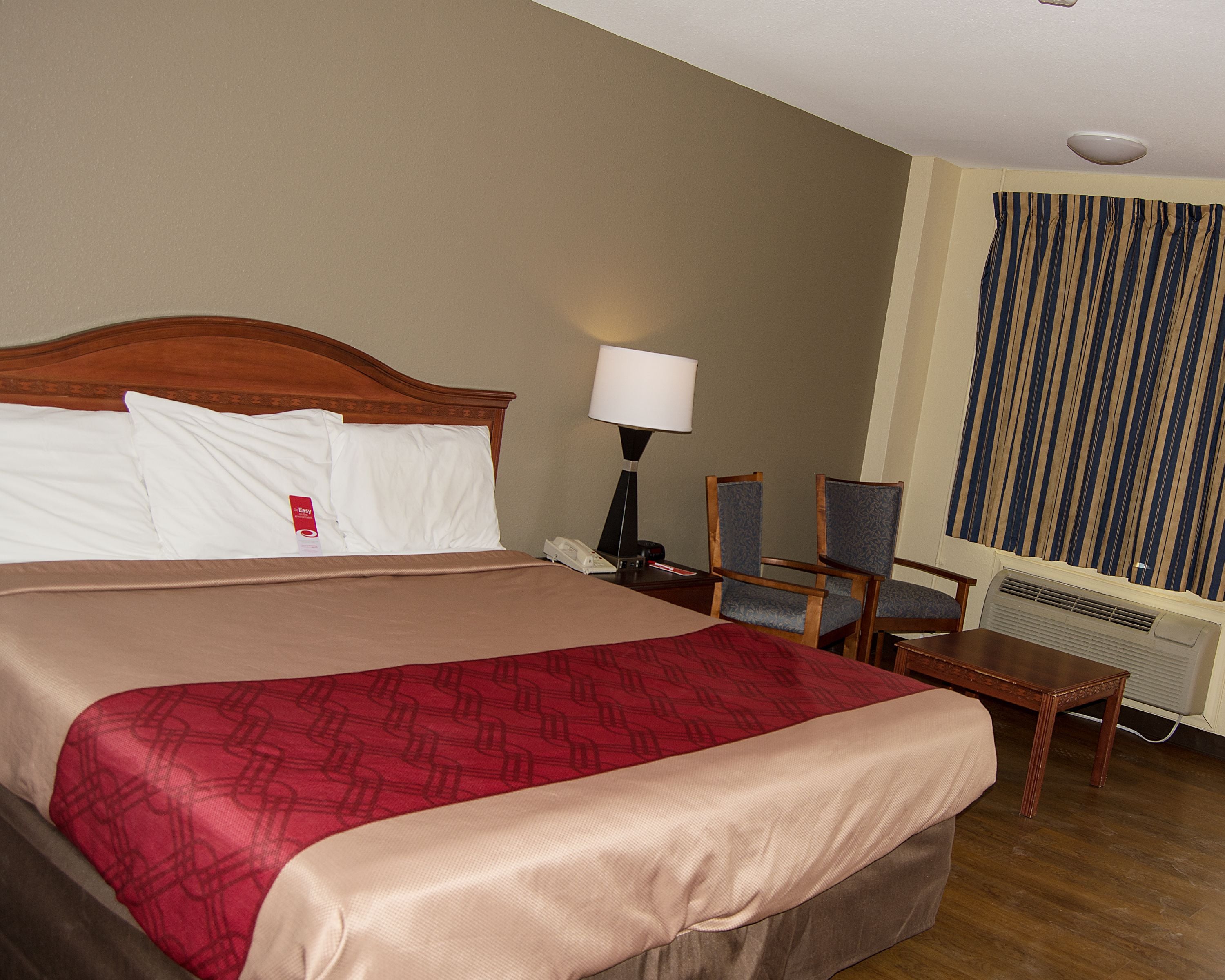 A hotel room with a large bed, a bedside table with a lamp, a chair, and a window with curtains.